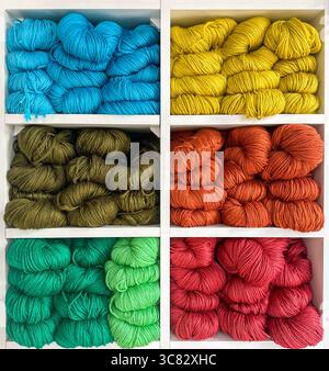 vibrant assortment of wool, wool blend, and cotton yarns in various colors neatly arranged on clean white shelves Stock Photo