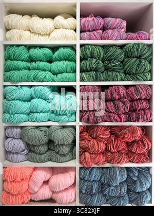 vibrant assortment of wool, wool blend, and cotton yarns in various colors neatly arranged on clean white shelves Stock Photo