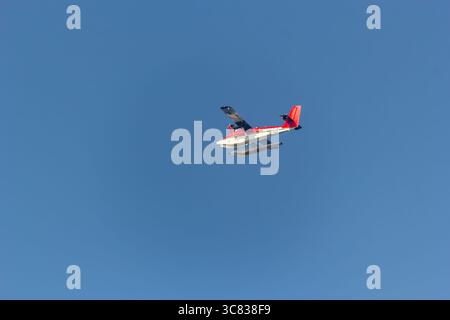 Red and white seaplane soars against a clear blue sky Stock Photo