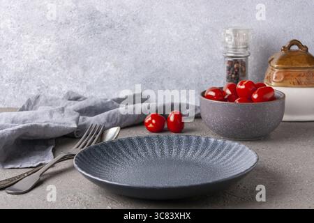 Empty plate, cutlery, bowl with cherry tomatoes on gray background Stock Photo