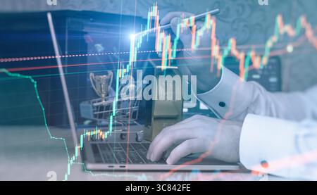 Businessman analyzing rising stock market chart on laptop, with a gold bar and trophy symbolizing financial success and smart investing. Stock Photo