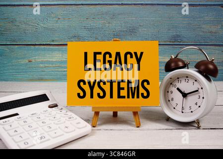 Legacy Systems text written on paper card with calculator and alarm clock on wooden background Stock Photo