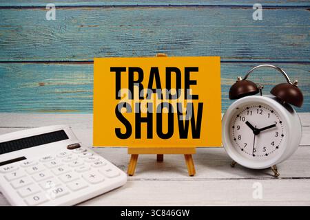 Trade Show text written on paper card with calculator and alarm clock on wooden background Stock Photo