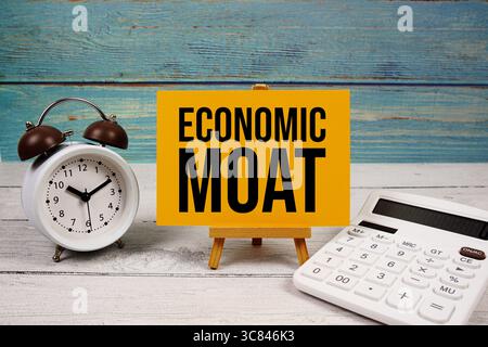 Economic Moat text written on paper card with calculator and alarm clock on wooden background Stock Photo