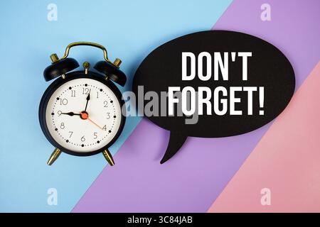 Don't Forget! text on speech bubble with alarm clock top view on blue, purple and pink geometric background Stock Photo