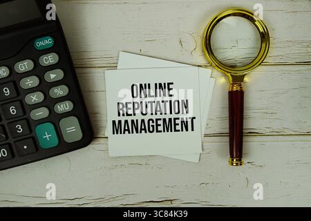 ORM (Online Reputation Management ) text message on sticky note with magnifying glass and calculator on wooden background Stock Photo