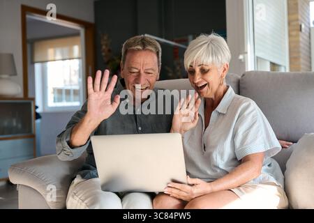 Happy senior couple video calling family with laptop at home Stock Photo