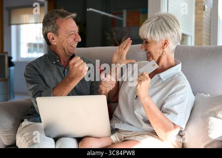 Happy senior couple shopping online using laptop and credit card at home Stock Photo