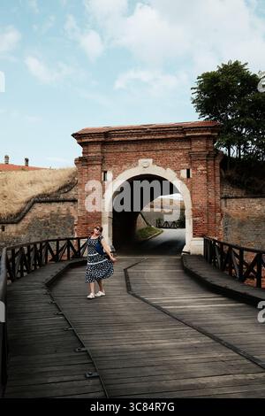 Woman posing on wooden bridge in front of arched gate of Petrovaradin Fortress, Novi Sad, Serbia. Travel concept. Stock Photo
