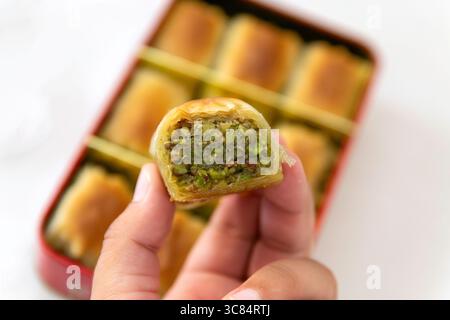 Close-Up of  Pistachio Baklava Held in Hand, Box of Sweets on white Background, flatlay, copy space Stock Photo