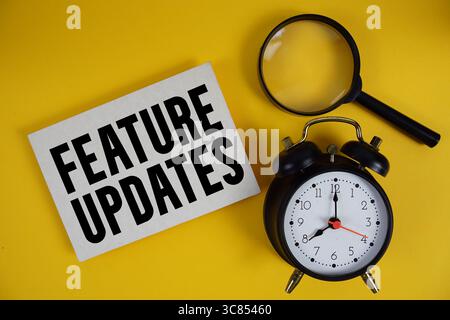 Feature Updates text written on paper with magnifying glass and alarm clock on yellow background Stock Photo