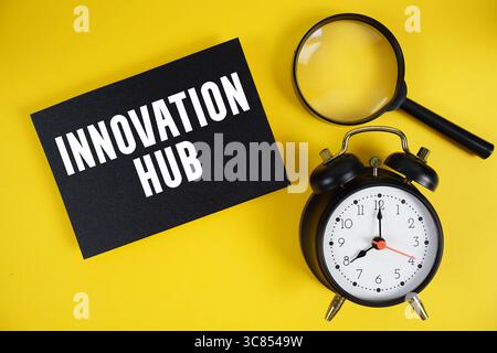 Innovation Hub text written on paper with magnifying glass and alarm clock on yellow background Stock Photo
