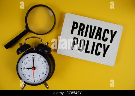 Privacy Policy text written on paper with magnifying glass and alarm clock on yellow background Stock Photo