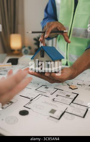 two architect is in office and sharing their strategy idea of building plan to each other, there are blueprint and house model on the desk in the offi Stock Photo
