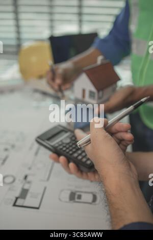 two architect is in office and sharing their strategy idea of building plan to each other, there are blueprint and house model on the desk in the offi Stock Photo