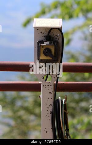 An outdoor electrical power switch stands mounted on a metal post, marked by signs of corrosion and bundled cables, likely used for switching heavy Stock Photo