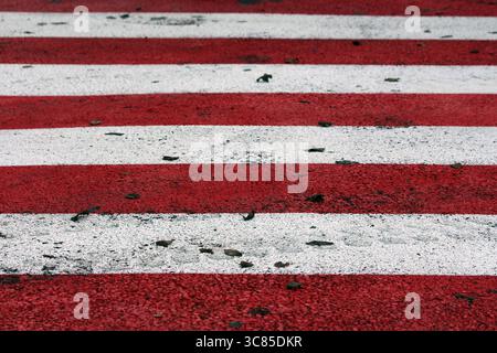 A close-up view of a zebra crossing with alternating red and white painted stripes on textured asphalt, scattered with small debris and road markings Stock Photo