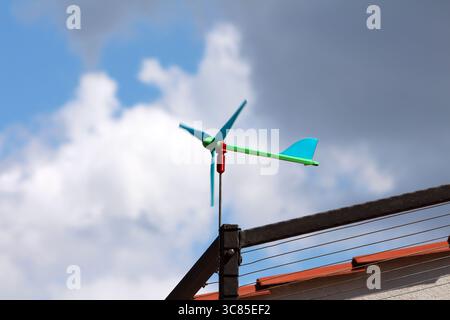 A compact plastic wind turbine is mounted on a rooftop metal pole, likely used for measuring wind speed or demonstrating small-scale renewable power Stock Photo
