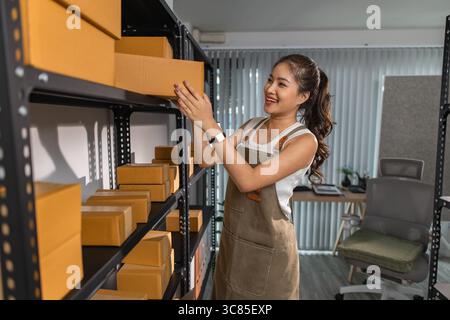 a female employee is checking parcel boxes in a warehouse, a warehouse manager is counting parcel boxes on shelves, a small online business owner is i Stock Photo