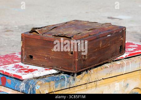 A battered, antique-style wooden box with warped panels, peeling surfaces, and visible distress marks, placed outdoors on colorful, paint-chipped Stock Photo