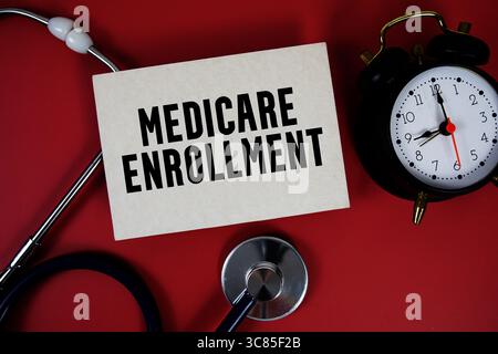 Medicare Enrollment text written on paper card with stethoscope on red background Stock Photo