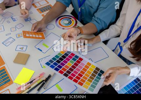 ux, ui, web and mobile app designers are discussing the look and feel of the website or app they are designing including color schemes and layouts to Stock Photo