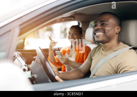 Young black couple driving car together and using smartphone Stock Photo