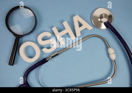 OSHA abbreviation of Occupational Safety and Health Administration alphabet letters with magnifying glass and stethoscope on blue background Stock Photo