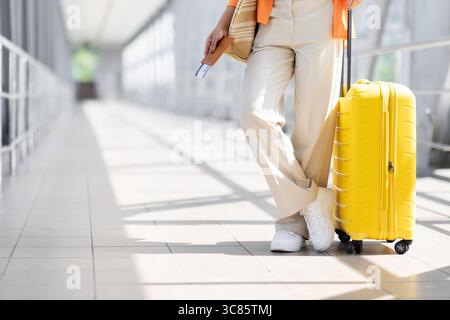 Cropped shot of young black woman standing with yellow suitcase at airport Stock Photo