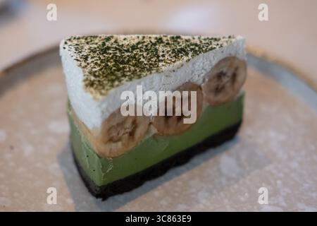 Matcha green tea banoffee pie, served on plate. It is a dessert made from banana, whipped cream, thick caramel sauce with crumbled base. Stock Photo