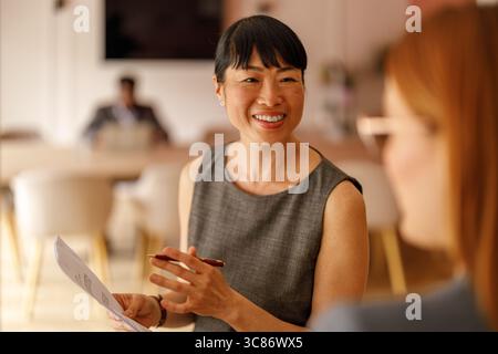 Successful female manager discussing project documents and sharing ideas with coworker in modern workplace Stock Photo