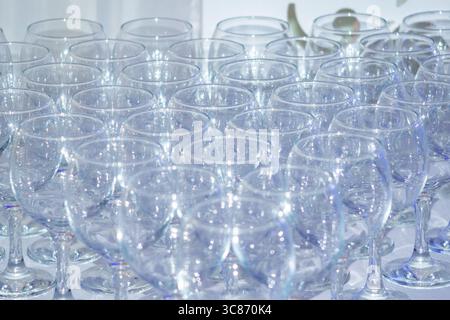 A large number of clear glassware is meticulously arranged on a table, ready for use at a formal gathering or event, glowing under soft lighting. Stock Photo