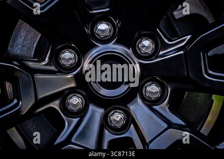 Detailed close-up of a modern black alloy wheel featuring metal lug nuts and a smooth, unbranded center cap. Ideal for use in automotive, engineering, Stock Photo