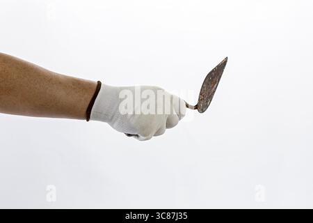 A hand wearing white rubber glove holds rusty trowel against plain background, suggesting focus on gardening or construction work Stock Photo