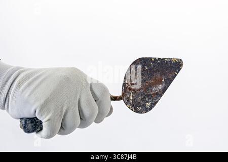 A hand in white rubber glove holds rusty metal trowel against plain background, suggesting focus on gardening or construction tools Stock Photo