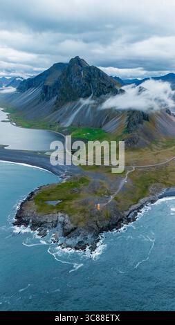 Immerse in the stunning Icelandic scenery showcasing towering mountains shrouded in clouds, rugged coastlines, and vibrant green landscapes. Hvalnes Nature Reserve Iceland Stock Photo