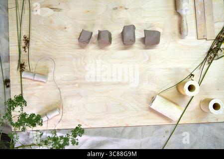 Clay cut into small pieces ready for shaping into napkin rings. Tools, greenery, and textured molds set on a wooden table create a natural and artisti Stock Photo