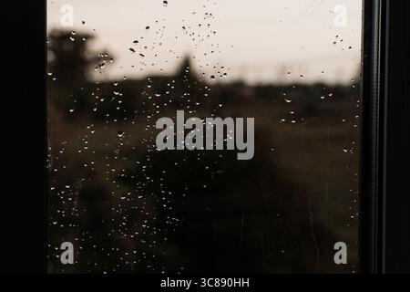 Atmospheric view through a wet window showing blurred tree silhouettes against a gray overcast sky, evoking a calm, melancholic mood, suitable for the Stock Photo