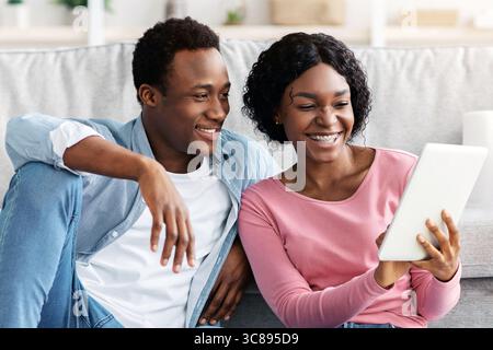 Black couple with cleaning tools resting, using digital tablet Stock Photo