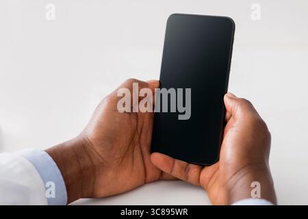 Online doctor and remote advice. Black man doctor using smartphone with blank screen, consulting patients distantly Stock Photo