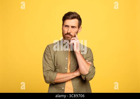 Thoughtful man reflecting against a bright yellow background in casual attire Stock Photo