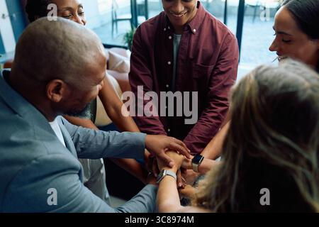 Diverse business people smiling while putting their arms together in office Stock Photo