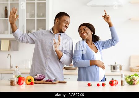 Positive pregnant black couple having fun while cooking Stock Photo