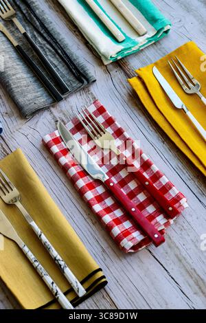 A flat lay arrangement of various forks and knives on different colored napkins and a rustic wooden background, showcasing diverse dining styles. Stock Photo
