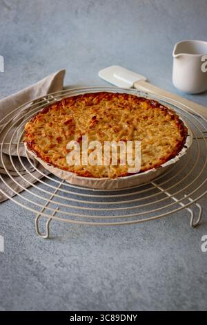 A freshly baked golden-brown pie or tart with a crumble topping, resting on a wire cooling rack on a rustic kitchen countertop. Stock Photo