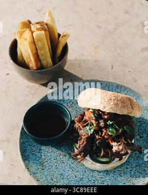 Plate of  BBQ pulled pork sandwich served with sauce and fried potatoes chips Stock Photo