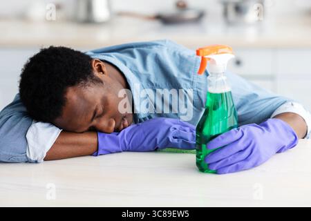 Tired black guy in gloves holding spray bottle, fell asleep Stock Photo