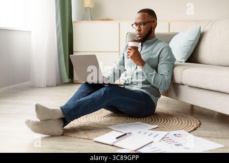 Black Man Working On Laptop Sitting On Floor At Home Stock Photo