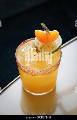 spicy orange-hued cocktail served on the rocks in a lowball glass, thoughtfully rimmed with chili-salt seasoning. Stock Photo