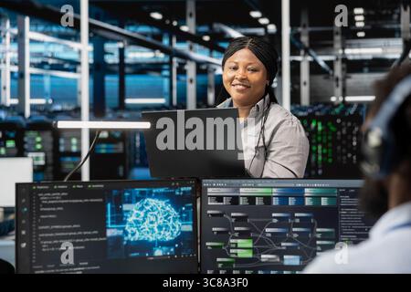 Portrait of smiling software developer working in data center with artificial intelligence tech to process massive datasets. Happy IT professional in server hub storing data used for deep learning Stock Photo